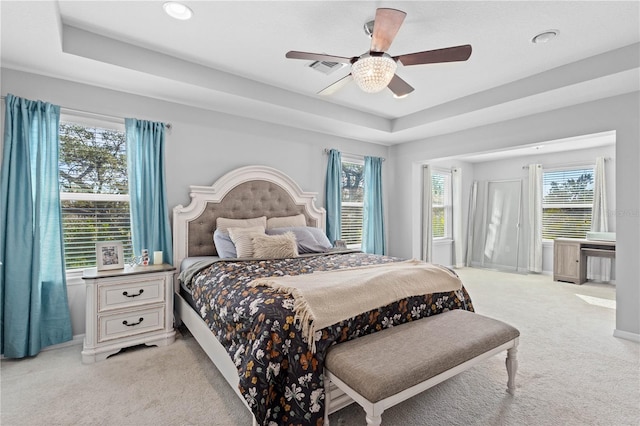 bedroom with light carpet, a tray ceiling, and ceiling fan