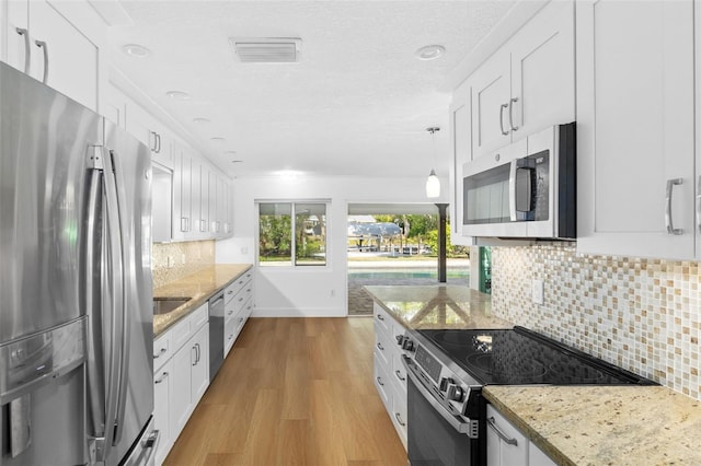 kitchen with appliances with stainless steel finishes, pendant lighting, white cabinets, light hardwood / wood-style floors, and light stone countertops