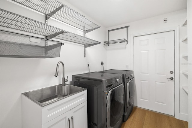 laundry room featuring sink, washer and clothes dryer, light hardwood / wood-style floors, and cabinets