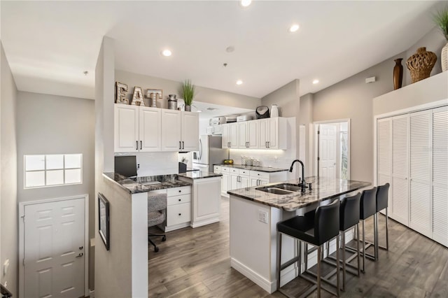 kitchen with a breakfast bar, stainless steel refrigerator, sink, white cabinets, and a center island with sink