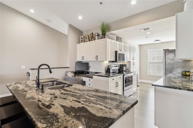 kitchen featuring sink, appliances with stainless steel finishes, dark stone counters, decorative backsplash, and white cabinets