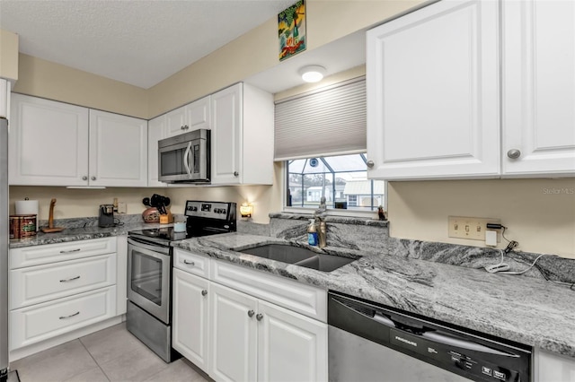 kitchen featuring sink, light tile patterned floors, appliances with stainless steel finishes, light stone counters, and white cabinets