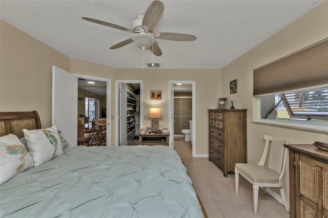 tiled bedroom with ensuite bathroom, a spacious closet, ceiling fan, and a textured ceiling