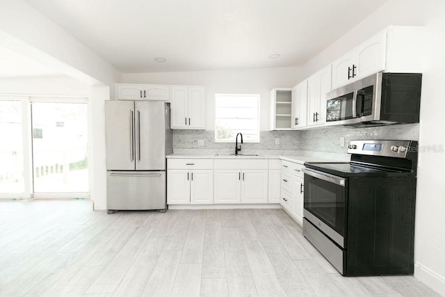 kitchen featuring sink, appliances with stainless steel finishes, white cabinetry, tasteful backsplash, and light wood-type flooring