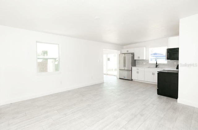 kitchen featuring sink, white cabinets, stainless steel fridge, decorative backsplash, and light hardwood / wood-style floors