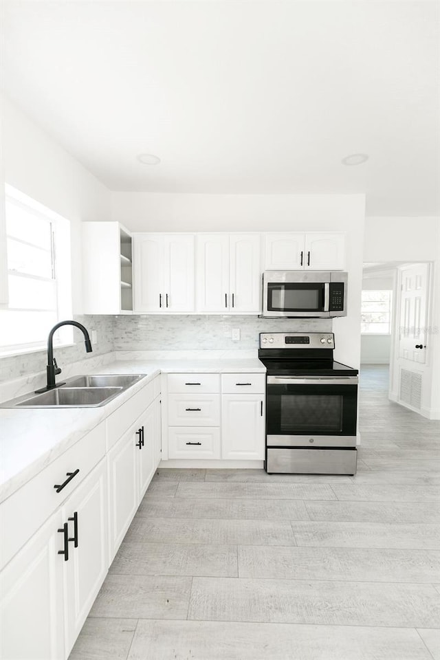 kitchen with tasteful backsplash, appliances with stainless steel finishes, sink, and white cabinets