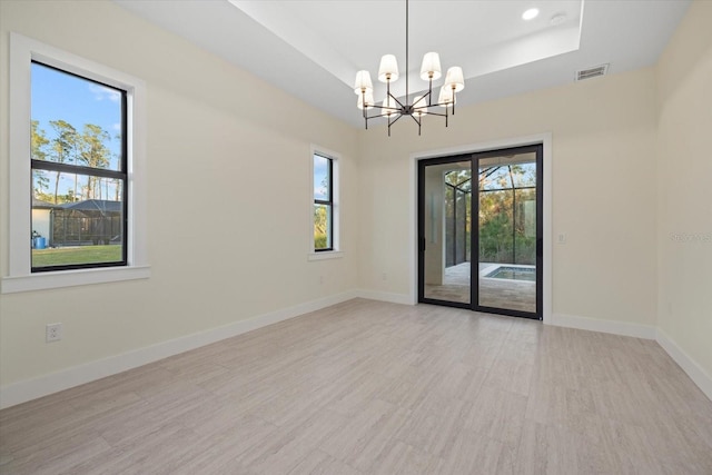 empty room featuring an inviting chandelier, a tray ceiling, and light hardwood / wood-style floors