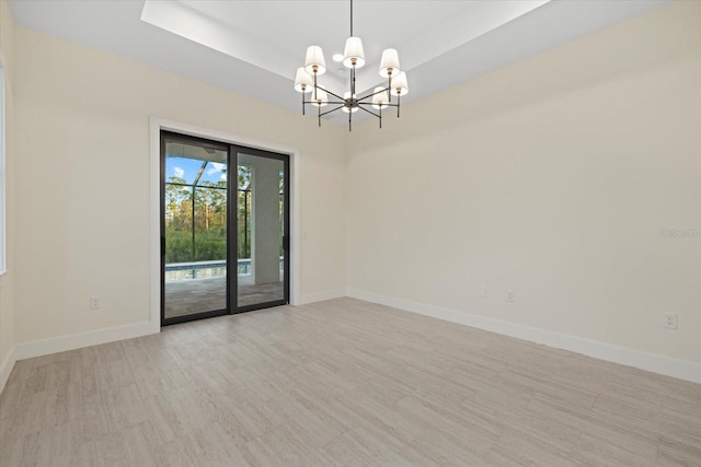 empty room with a tray ceiling, light hardwood / wood-style flooring, and a chandelier