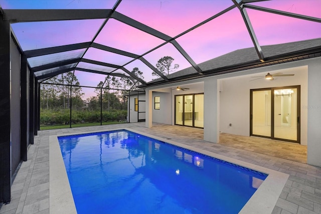 pool at dusk with a lanai, ceiling fan, and a patio area