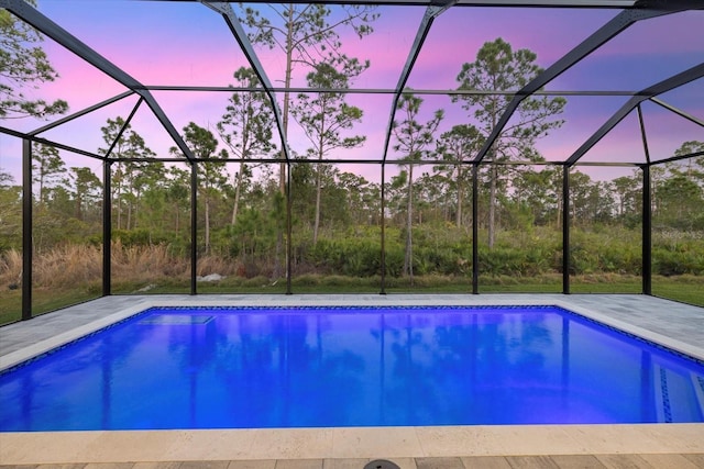 pool at dusk with glass enclosure and a patio area