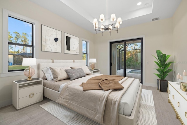 bedroom featuring an inviting chandelier, a tray ceiling, access to exterior, and light wood-type flooring