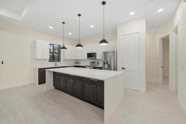 kitchen with sink, stainless steel appliances, a center island, white cabinets, and decorative light fixtures