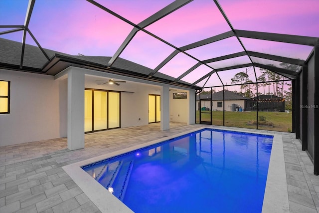 pool at dusk featuring a lanai, ceiling fan, and a patio area