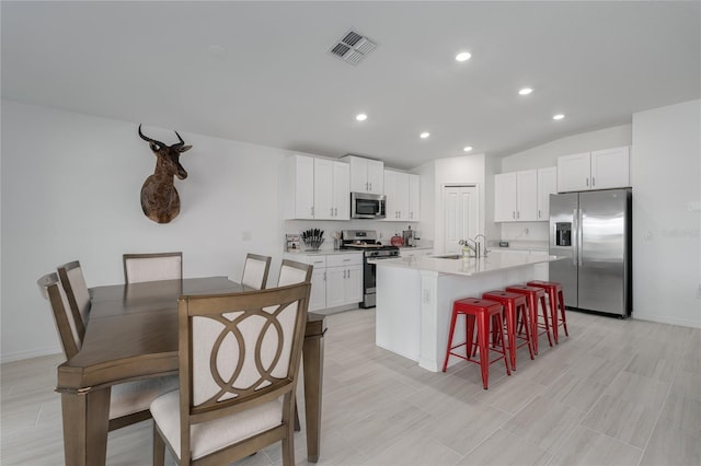 kitchen featuring a kitchen island with sink, white cabinetry, a kitchen breakfast bar, and appliances with stainless steel finishes