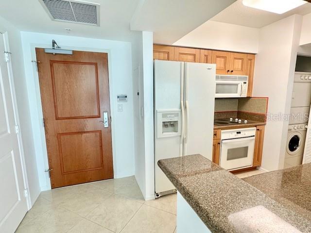 kitchen featuring light tile patterned floors, white appliances, and stacked washer and clothes dryer