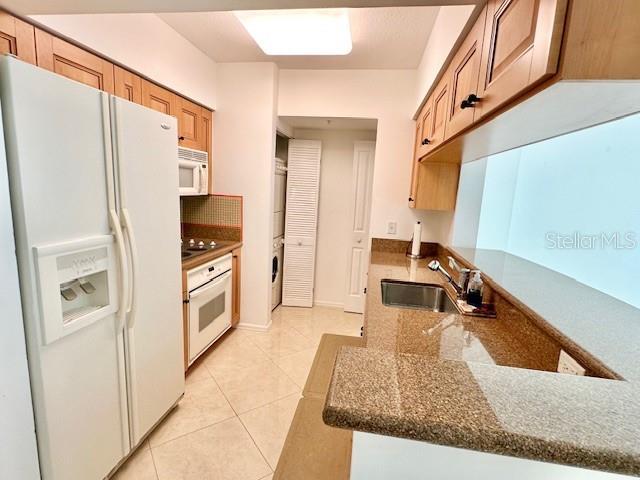 kitchen with light tile patterned flooring, sink, dark stone counters, kitchen peninsula, and white appliances