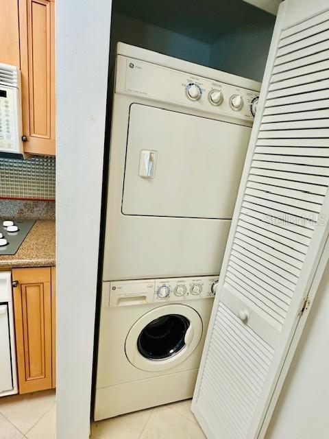 clothes washing area featuring light tile patterned flooring and stacked washer and clothes dryer