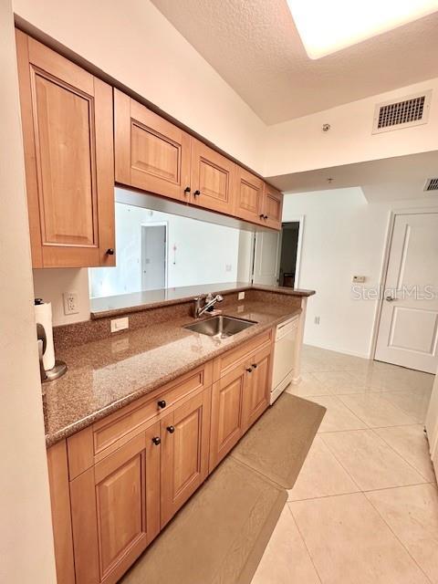 kitchen with sink, a textured ceiling, light tile patterned floors, dishwasher, and stone counters