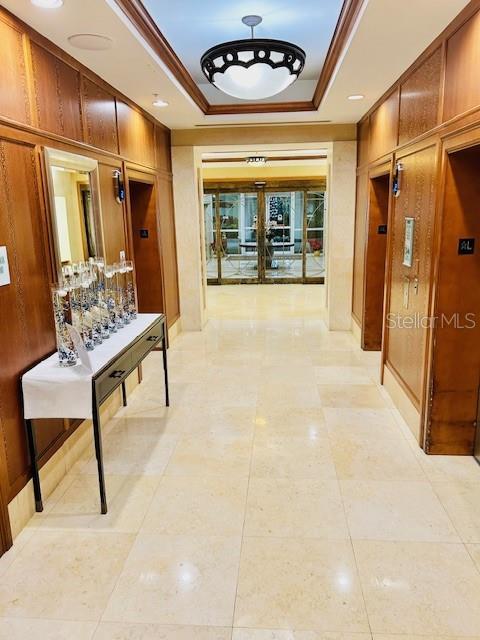 hallway featuring light tile patterned flooring, ornamental molding, wooden walls, and a raised ceiling