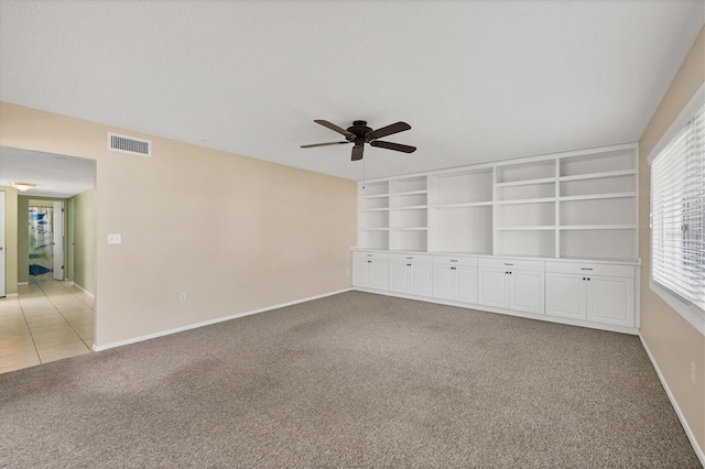 unfurnished room with ceiling fan, built in features, light carpet, and a textured ceiling