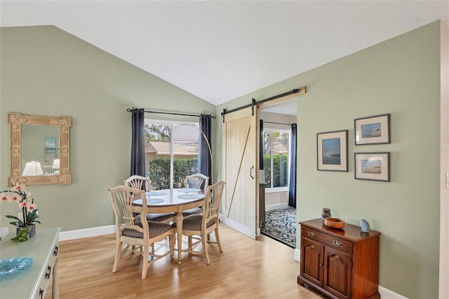 dining space with vaulted ceiling, a barn door, and light hardwood / wood-style flooring