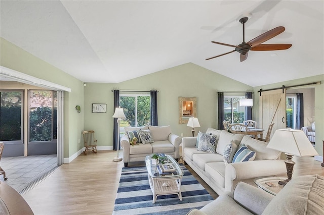 living room featuring ceiling fan, a barn door, light hardwood / wood-style floors, and lofted ceiling