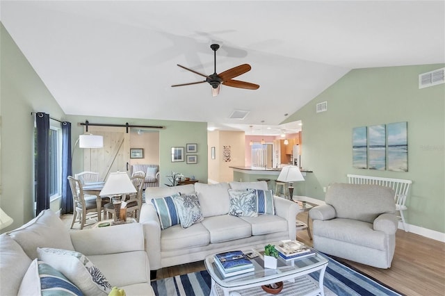 living room featuring vaulted ceiling, ceiling fan, a barn door, and hardwood / wood-style flooring