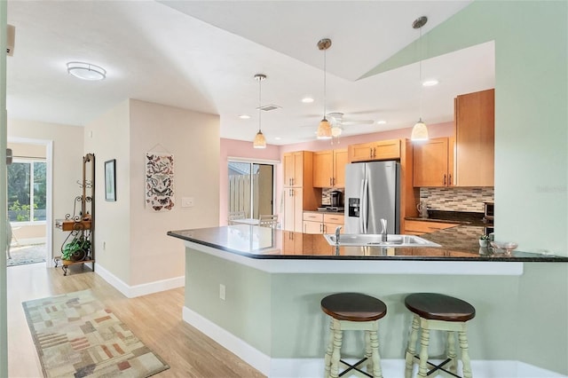 kitchen with sink, pendant lighting, stainless steel fridge with ice dispenser, kitchen peninsula, and tasteful backsplash