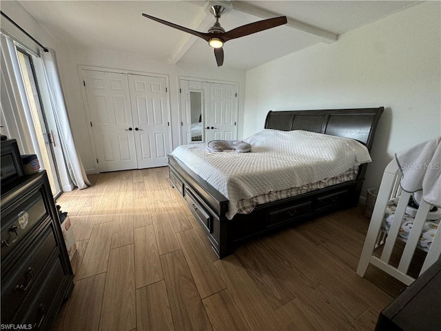 bedroom with ceiling fan, two closets, wood-type flooring, and beamed ceiling