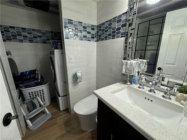 bathroom featuring toilet, washer / dryer, tile walls, vanity, and hardwood / wood-style flooring