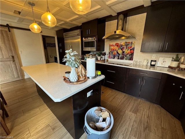 kitchen with backsplash, coffered ceiling, built in appliances, a barn door, and wall chimney range hood