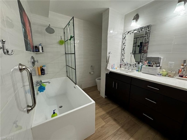 bathroom featuring toilet, wood-type flooring, tile walls, vanity, and a tub