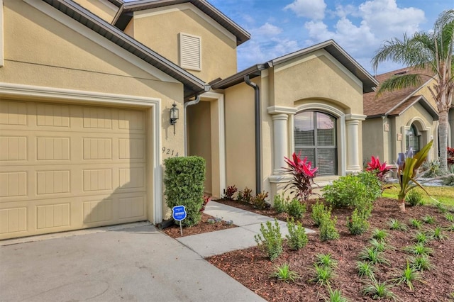 view of exterior entry featuring concrete driveway, a garage, and stucco siding