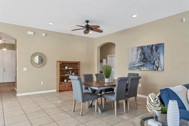 dining room with light tile patterned floors, baseboards, arched walkways, and a ceiling fan