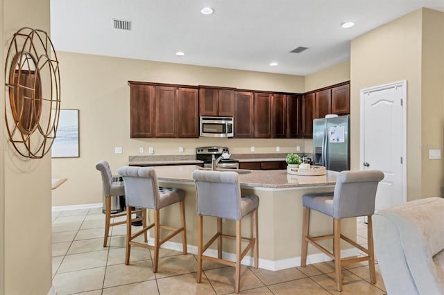 kitchen featuring dark brown cabinetry, visible vents, a breakfast bar area, and stainless steel appliances