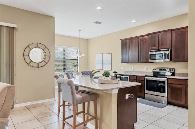 kitchen with a breakfast bar area, visible vents, light tile patterned flooring, an island with sink, and stainless steel appliances