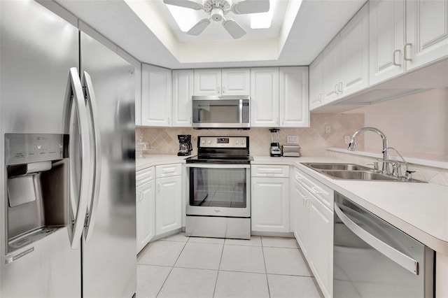 kitchen with sink, light tile patterned floors, a raised ceiling, stainless steel appliances, and white cabinets