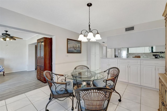 tiled dining area with ceiling fan with notable chandelier and a textured ceiling