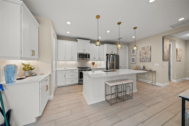 kitchen featuring a kitchen bar, white cabinetry, a center island with sink, appliances with stainless steel finishes, and pendant lighting