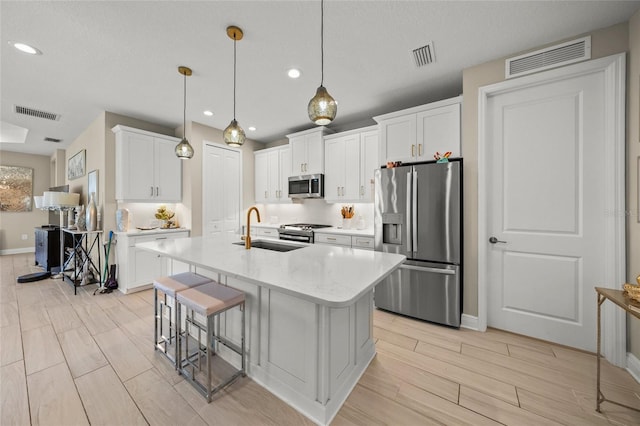 kitchen featuring sink, appliances with stainless steel finishes, hanging light fixtures, white cabinets, and a center island with sink