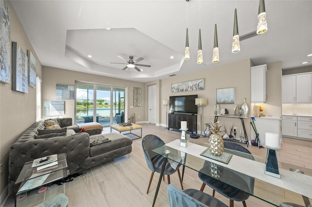 living room with light hardwood / wood-style flooring, ceiling fan, and a tray ceiling