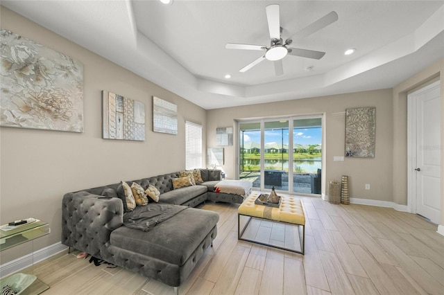 living room featuring a tray ceiling, light wood-type flooring, ceiling fan, and a water view