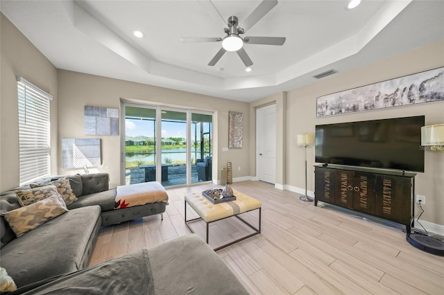 living room with light hardwood / wood-style flooring, a raised ceiling, and ceiling fan