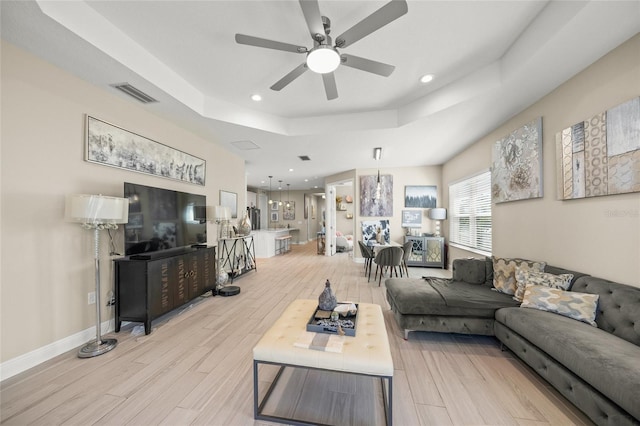 living room with ceiling fan, a raised ceiling, and light hardwood / wood-style flooring