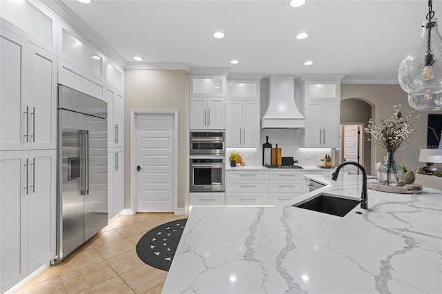 kitchen featuring premium range hood, pendant lighting, sink, white cabinets, and stainless steel appliances