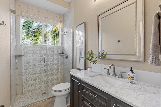 bathroom featuring vanity, a tile shower, tile patterned floors, and toilet