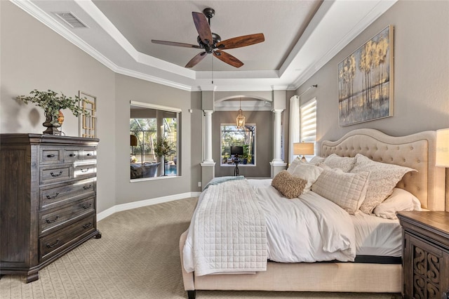 carpeted bedroom with ornamental molding, a tray ceiling, decorative columns, and multiple windows