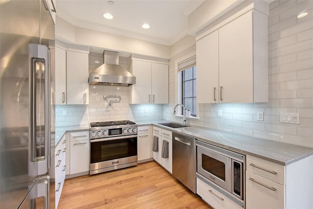 kitchen with wall chimney exhaust hood, sink, white cabinetry, appliances with stainless steel finishes, and light hardwood / wood-style floors