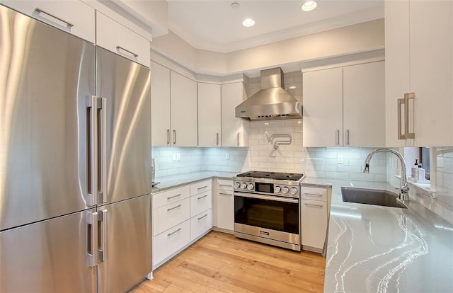 kitchen featuring wall chimney range hood, sink, white cabinets, and appliances with stainless steel finishes