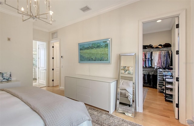 bedroom with crown molding, an inviting chandelier, a walk in closet, a closet, and light wood-type flooring